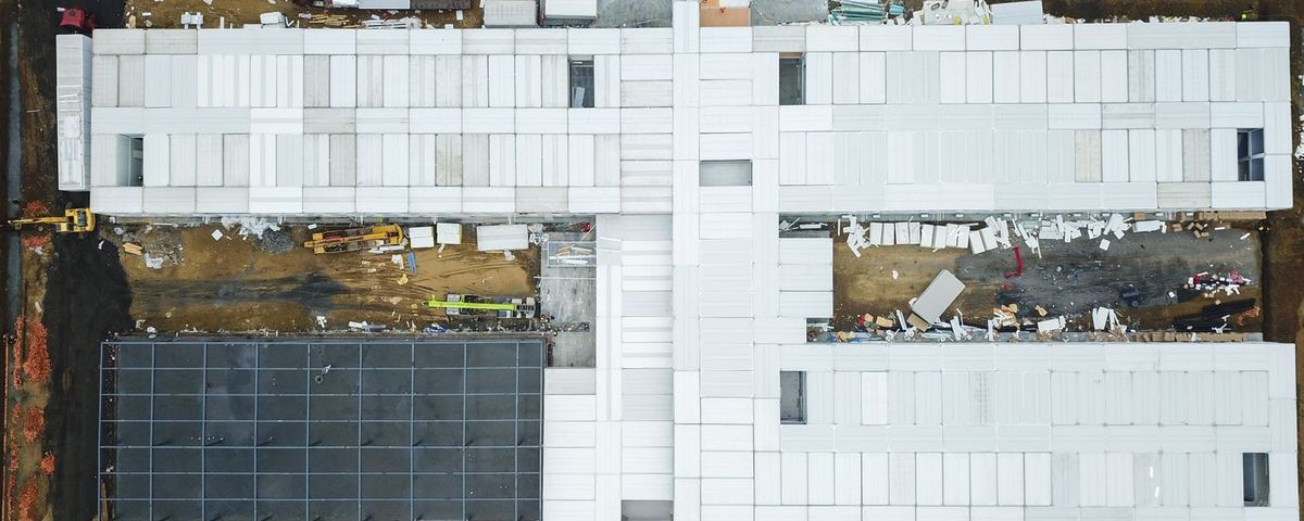 Aerial view of a large building under construction with cranes, deliveries and laydown areas