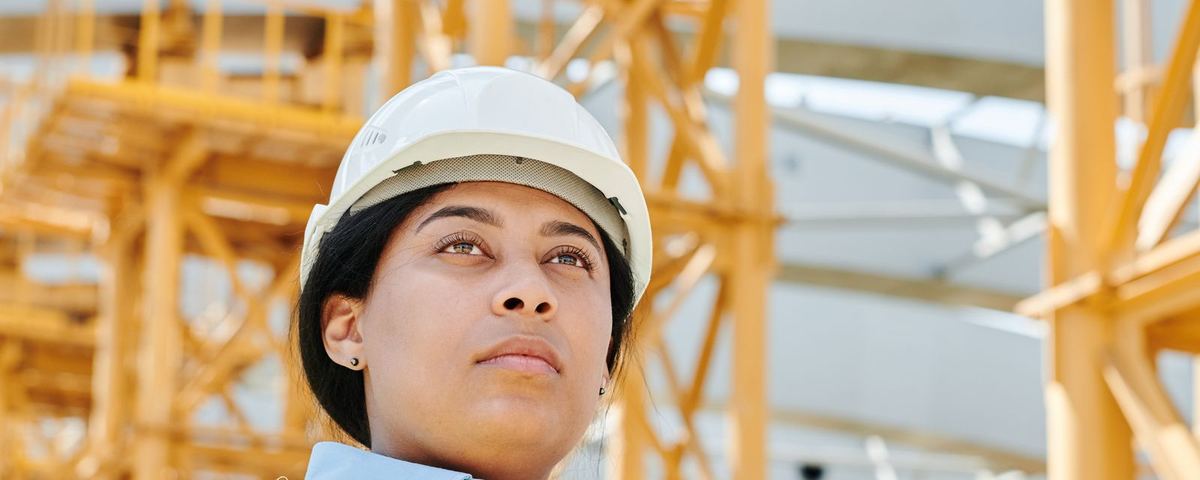 Quality engineer in hard hat and hi-vis with a clipboard in front of a steel frame