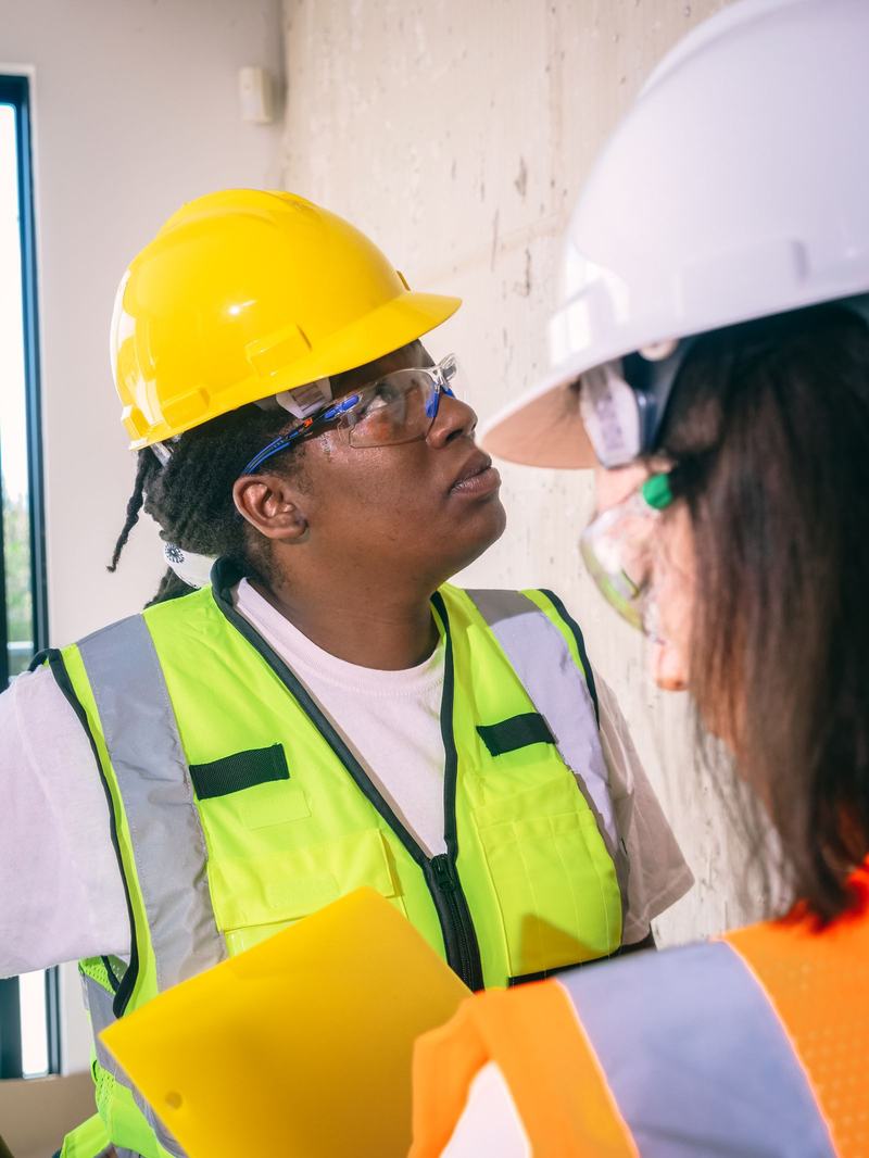 Two engineers in hard hats, safety glasses and hi-vis inspecting a wall during a site walk