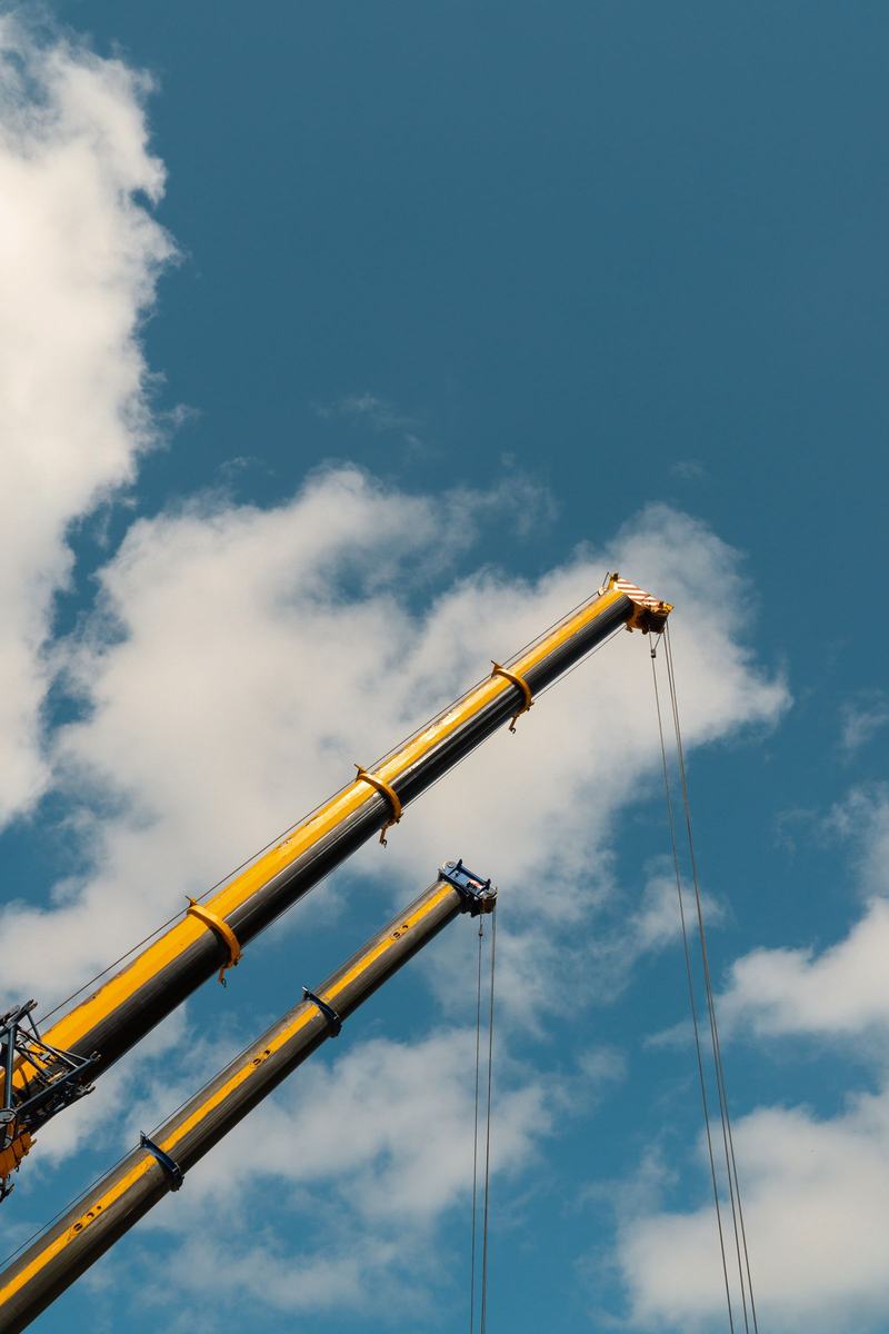 Two mobile crane booms extended against a blue sky