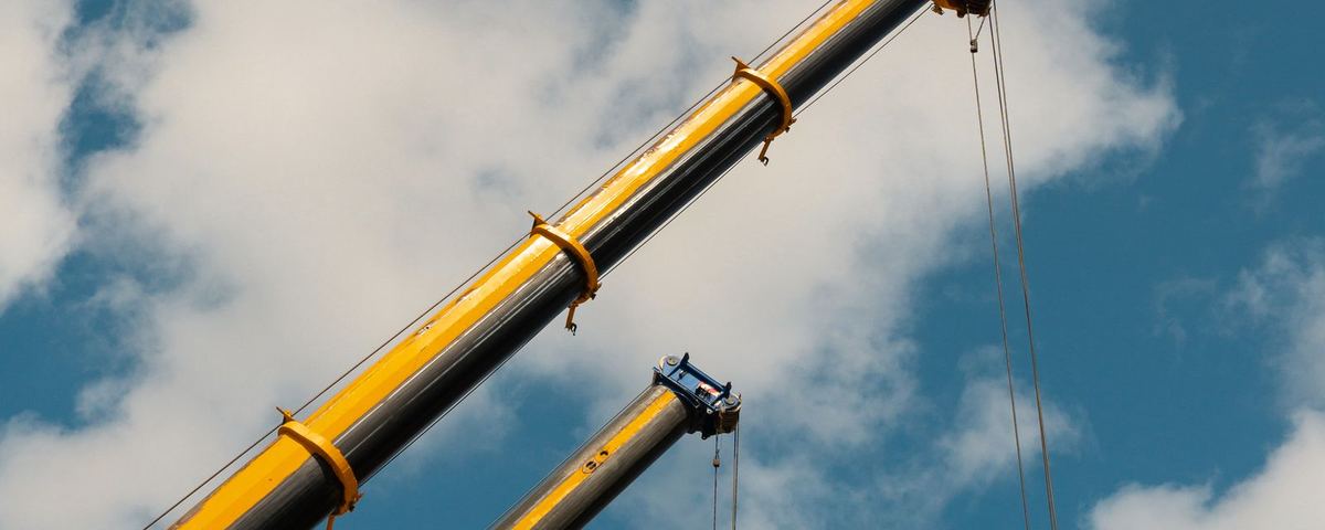 Two mobile crane booms extended against a blue sky
