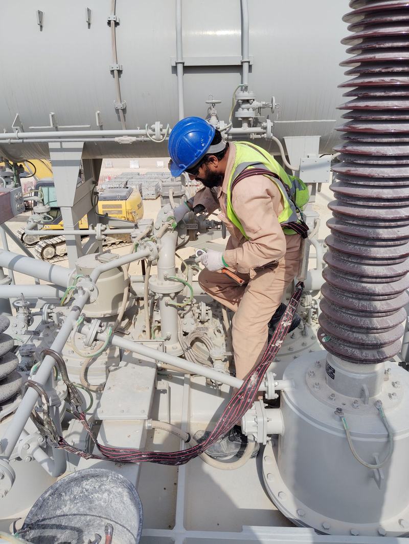 Electrical engineer in hard hat, hi-vis, gloves and harness working on a transformer bushing