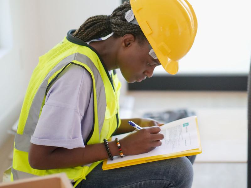 Engineer in hard hat, safety glasses and hi-vis completing an inspection record on a clipboard