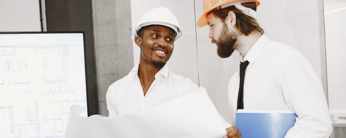 Two engineers in hard hats reviewing a drawing in a site office