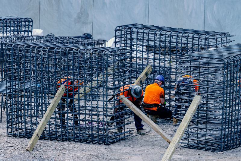 Steel fixers in hard hats and hi-vis tying prefabricated reinforcement cages