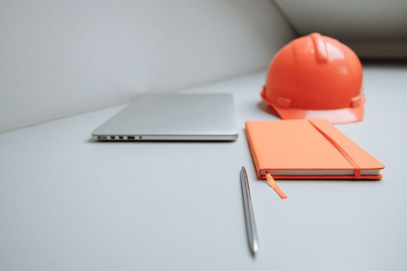 Laptop, notebook, pen and hard hat on a site office desk