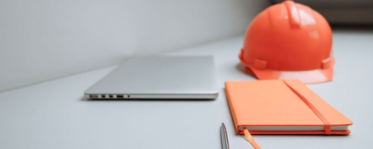 Laptop, notebook, pen and hard hat on a site office desk