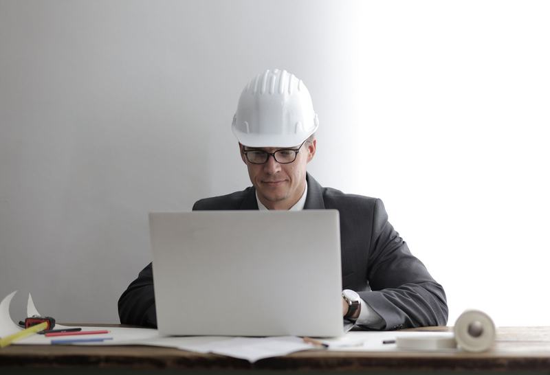 Engineer in a hard hat working at a laptop over drawings in a site office
