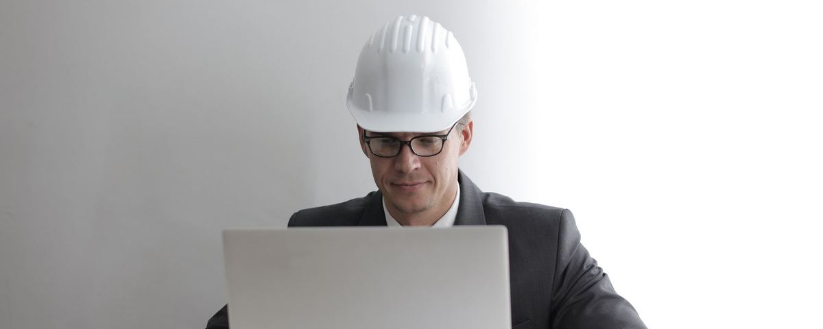 Engineer in a hard hat working at a laptop over drawings in a site office