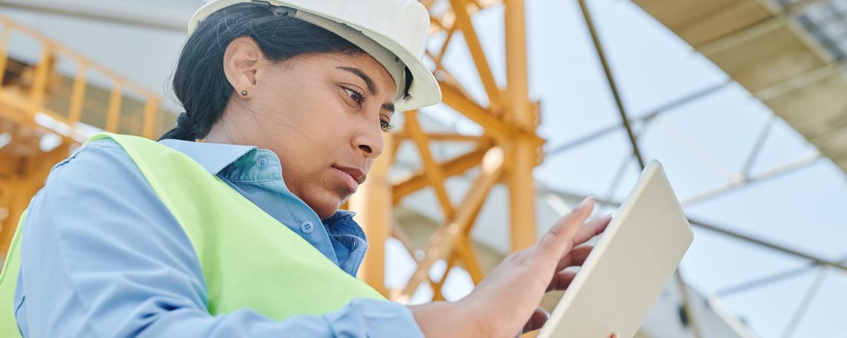 Engineer in hard hat and hi-vis using a tablet beneath a steel frame