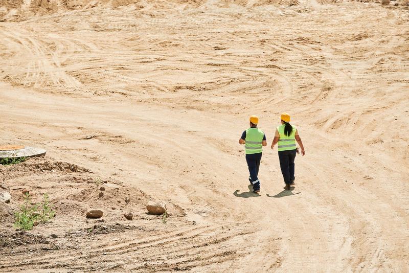Two engineers in hard hats and hi-vis walking across an earthworks site