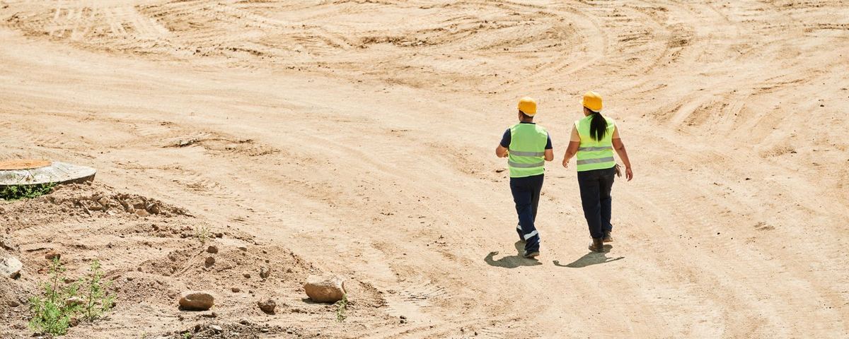 Two engineers in hard hats and hi-vis walking across an earthworks site