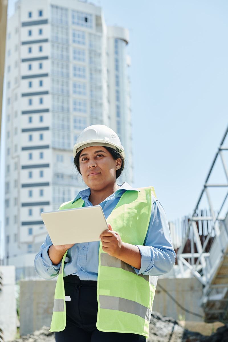 Site engineer in hard hat and hi-vis recording a check on a tablet on a city-centre site
